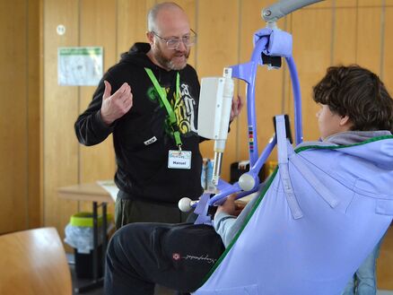 Mann zeigt einem Jungen Hilfsmittel für Schwerstbehinderte